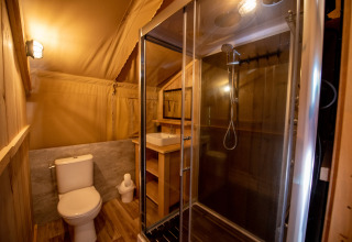 Baño dentro de una tienda safari en Camping Fargogne, Francia, con ducha, inodoro y lavabo de madera.