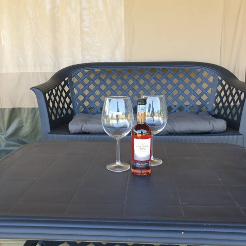 Botella de vino y dos copas sobre una mesa frente a un banco en Safari tent, ideal para relajarse.