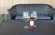Botella de vino y dos copas sobre una mesa frente a un banco en Safari tent, ideal para relajarse.