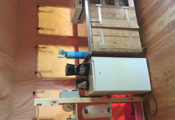 Petit espace cuisine dans une tente safari, avec mini-réfrigérateur, cafetière et placard en bois.