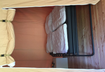 Vista interna di una tenda safari con due letti singoli, piumini e pavimento in legno.