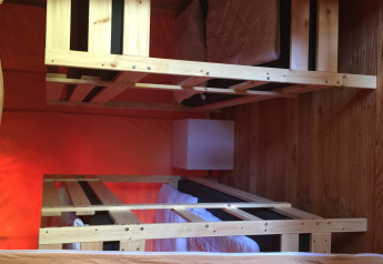 Interno di una tenda safari con due letti a castello in legno, lenzuola bianche, cuscini e pavimento in legno.