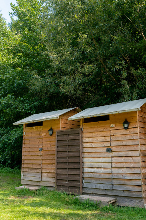 Twee aparte houten sanitairhutten met witte daken op Camping Bockenauer Schweiz in Duitsland, omgeven door bomen.