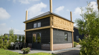Lodge Vakantiehuisje hooiberg con exterior de madera negra, techo de paja y área de terraza exterior.