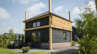 Udsigt til Vakantiehuisje hooiberg lodge med sort træbeklædning, stråtag og udendørs siddeplads.