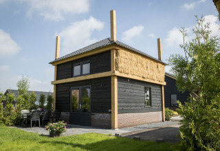 Vakantiehuisje hooiberg lodge with black wooden exterior, straw insulation and outdoor patio area visible.