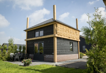 Vakantiehuisje hooiberg lodge with black wooden exterior, straw insulation and outdoor patio area visible.