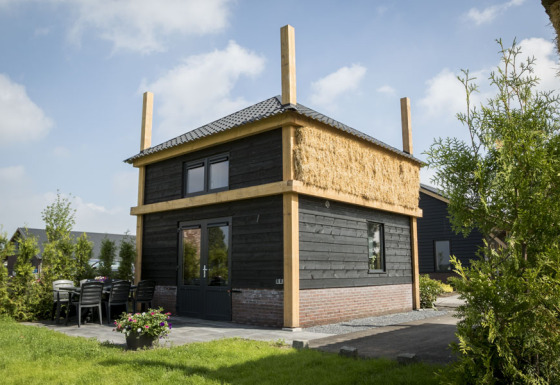 Vakantiehuisje hooiberg lodge with black wooden exterior, straw insulation and outdoor patio area visible.