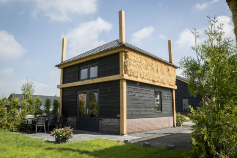 Vakantiehuisje hooiberg lodge con esterno in legno scuro, tetto di paglia e area patio all'aperto.