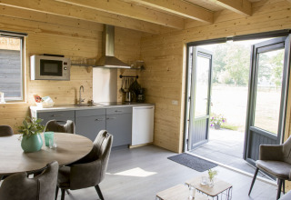 Modern vacation lodge kitchen and dining area with wood interior, open to patio, at Nieuw Romalo, Netherlands.