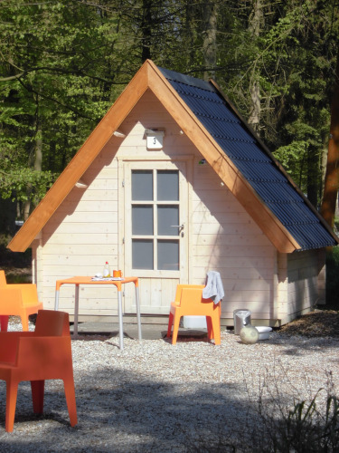 Kleine Holzhütte mit orangen Stühlen und Tisch davor, umgeben von Wald, bei Kabouterhuisje-Lodge.