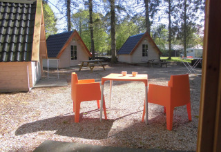 Außenbereich mit orangefarbenen Stühlen und Tisch vor Holzhütten im Kabouterhuisje, 't Urkerbos, Niederlande.