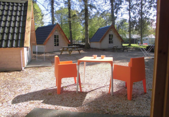 Outdoor area with orange chairs and table in front of wooden cabins at Kabouterhuisje, 't Urkerbos, Netherlands.