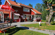 Red holiday house with outdoor seating and sun umbrella at Camping Falkudden in Dalarna, Sweden, on a sunny day.