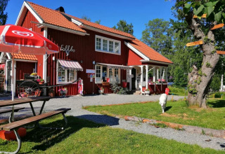 Red holiday house with outdoor seating and sun umbrella at Camping Falkudden in Dalarna, Sweden, on a sunny day.