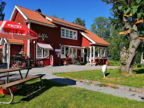 Rood vakantiehuis met buitenzitje en parasol bij Camping Falkudden in Dalarna, Zweden, op een zonnige dag.