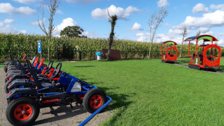 Toy pedal cars and a red play train on grass at Camping Nieuw Romalo holiday park, Gelderland, Netherlands