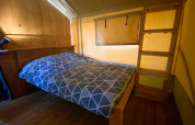 Interior de una tienda safari con cama doble, pared de madera, escalera y cálida iluminación amarilla.