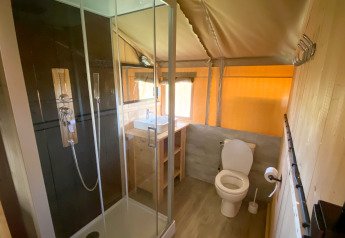 Badeværelse i et glamping-telt med moderne bruser, toilet og håndvask i naturligt træs interiør.
