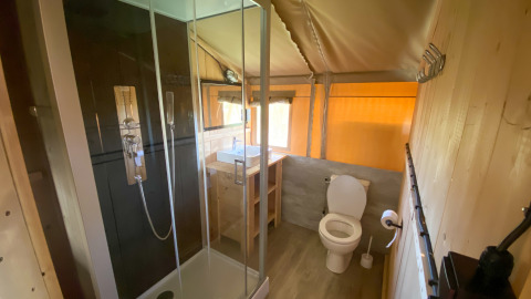 Baño en alojamiento glamping con ducha moderna, inodoro y lavabo de madera junto a una ventana.
