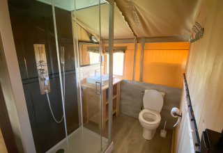 Badeværelse i et glamping-telt med moderne bruser, toilet og håndvask i naturligt træs interiør.