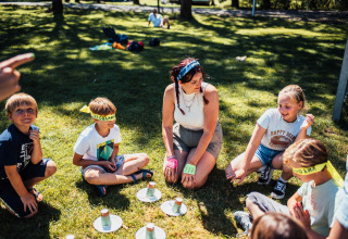 Children and a woman play a group game outdoors on the grass at Eurocamping Vessem BV in North Brabant, Netherlands.