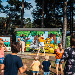 Niños participan en una actividad al aire libre frente a una cabaña pintada en Eurocamping Vessem, Brabante Norte.