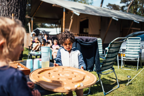 Kinderen spelen een bordspel buiten bij Eurocamping Vessem in Noord-Brabant, Nederland, met tenten achterin.