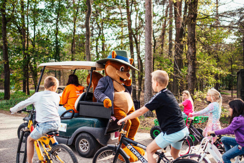Children biking around a mascot in a golf cart at Eurocamping Vessem holiday park, North-Brabant, Netherlands.
