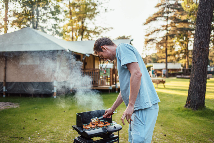 Hombre asando comida al aire libre en Eurocamping Vessem BV, parque vacacional en Brabante Septentrional, Países Bajos.