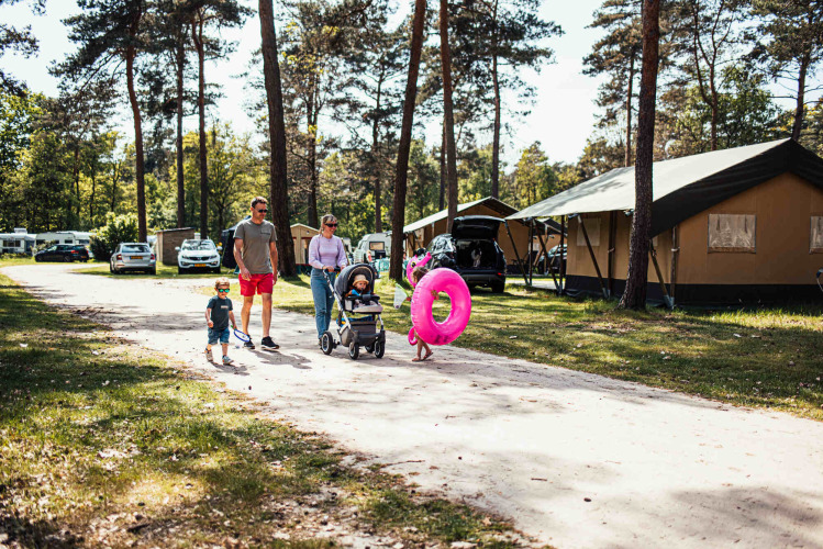 Familia caminando por Eurocamping Vessem BV, un parque de vacaciones en Brabante Septentrional, Países Bajos, con tiendas al fondo.