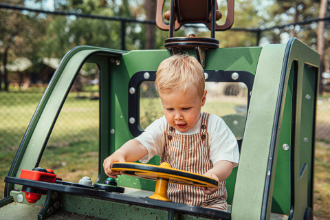 Bambino gioca su una macchina verde giocattolo a Eurocamping Vessem BV, parco vacanze nei Paesi Bassi.