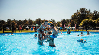 Niños divirtiéndose en la piscina exterior de Eurocamping Vessem BV en North Brabant, Países Bajos, un día soleado.