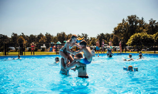 Niños divirtiéndose en la piscina exterior de Eurocamping Vessem BV en North Brabant, Países Bajos, un día soleado.