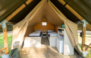 Vue intérieure d'une tente safari avec deux lits simples, plancher en bois et étagères de rangement à Vessem.