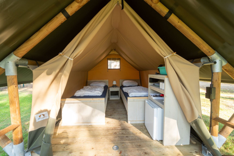 Vista interior de una tienda safari con dos camas individuales, suelo de madera y estanterías de almacenamiento.