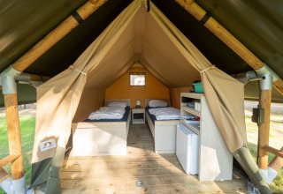 Vista interior de una tienda safari con dos camas individuales, suelo de madera y estanterías de almacenamiento.