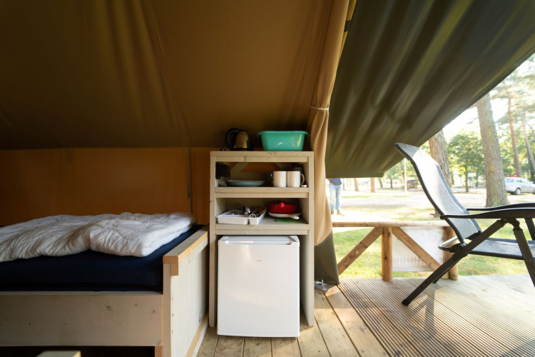 Interior de tienda safari en Eurocamping Vessem, Países Bajos, con cama, mini nevera y estantería.