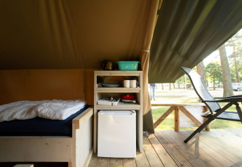 Interior de tienda safari en Eurocamping Vessem, Países Bajos, con cama, mini nevera y estantería.