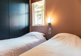 Acogedor dormitorio con dos camas individuales, ventana y lámpara en Boslodge de Eurocamping Vessem, Países Bajos.