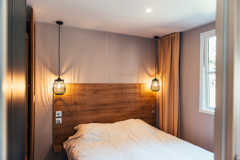 Dormitorio moderno en Boslodge, Eurocamping Vessem BV, Países Bajos, con cabecera de madera y luces colgantes.