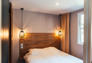 Dormitorio moderno en Boslodge, Eurocamping Vessem BV, Países Bajos, con cabecera de madera y luces colgantes.