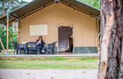 Mujer leyendo frente a una tienda Safari en Eurocamping Vessem BV, Países Bajos, rodeada de naturaleza.