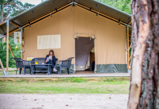 Mujer leyendo frente a una tienda Safari en Eurocamping Vessem BV, Países Bajos, rodeada de naturaleza.
