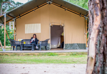 Mujer leyendo frente a una tienda Safari en Eurocamping Vessem BV, Países Bajos, rodeada de naturaleza.