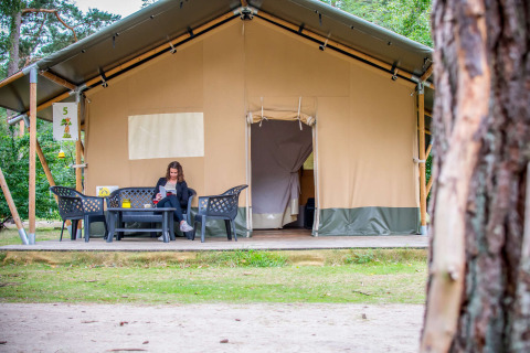 En kvinde læser foran en Safari-telt lodge på Eurocamping Vessem BV i Holland, omgivet af natur.