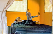 Niño despertando en la cama con peluches dentro de una tienda safari en Eurocamping Vessem BV, Países Bajos.