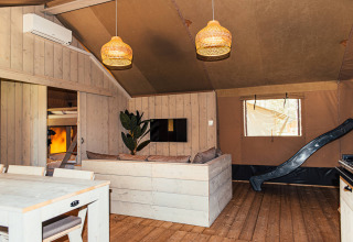 Interieur van een safaritent met houten afwerking, zithoek, eethoek en glijbaan bij Eurocamping Vessem.