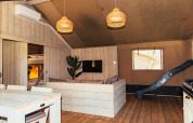 Intérieur d'une tente safari avec murs en bois, canapé, salle à manger et toboggan à Eurocamping Vessem.