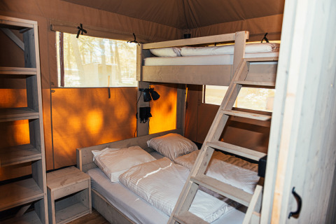 Vista interior de la tienda Safari + sanitario en Eurocamping Vessem BV, con literas y estanterías de madera.